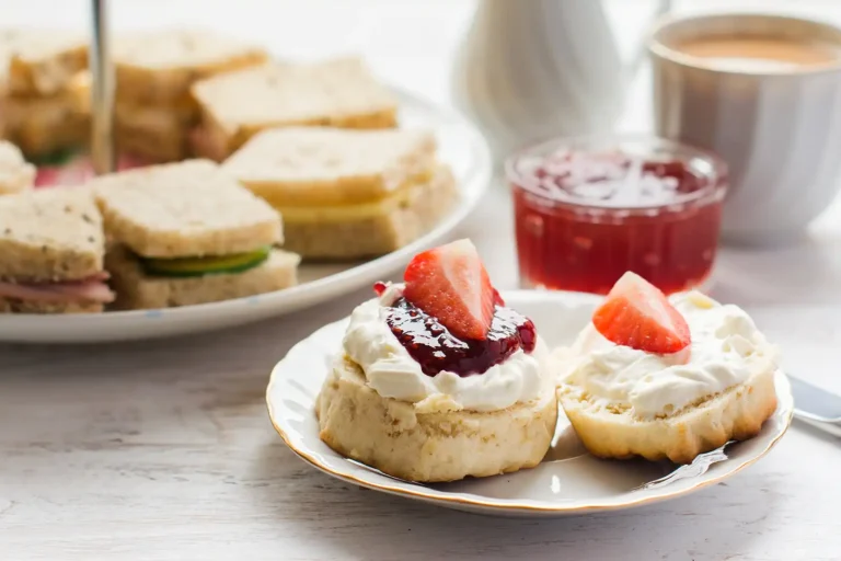 Scones with clotted cream, jam, and strawberries in front of finger sandwiches.