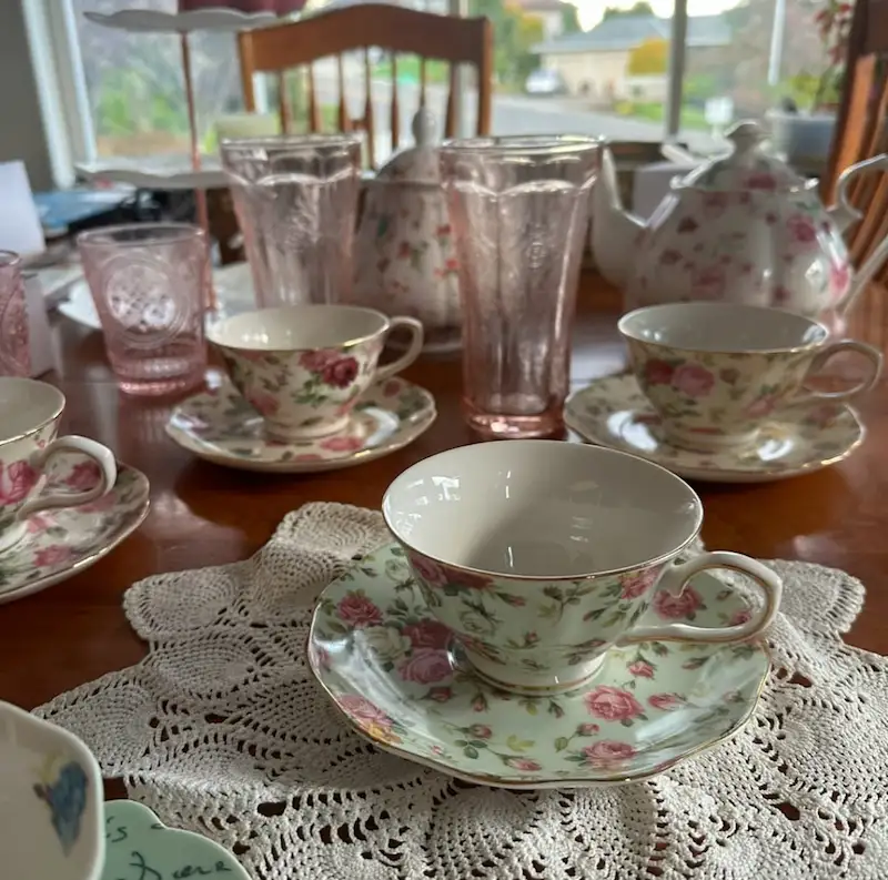 Assortment of pink and green tea sets on a table with knitted doilies